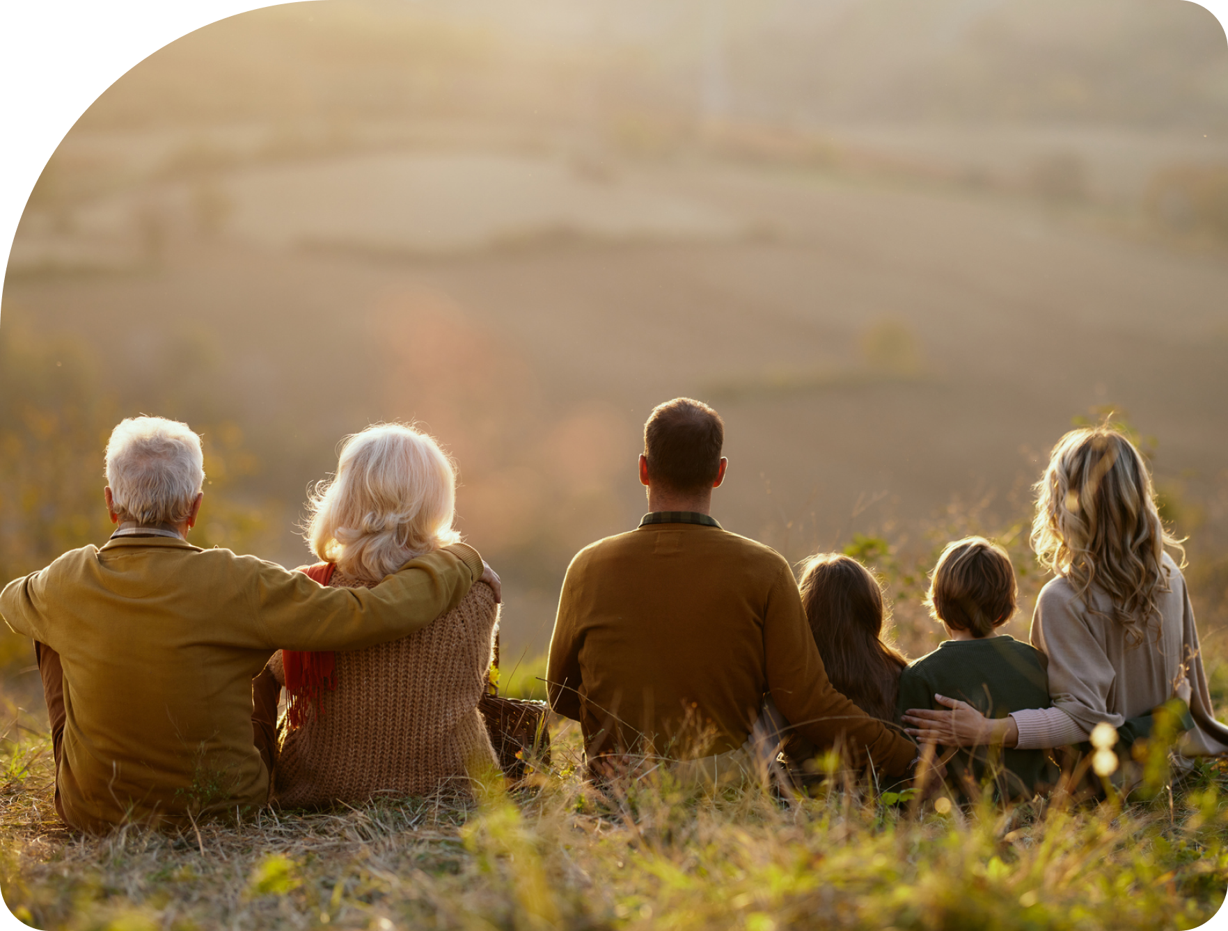 A loving generational family sitting on a hill watching the sunset